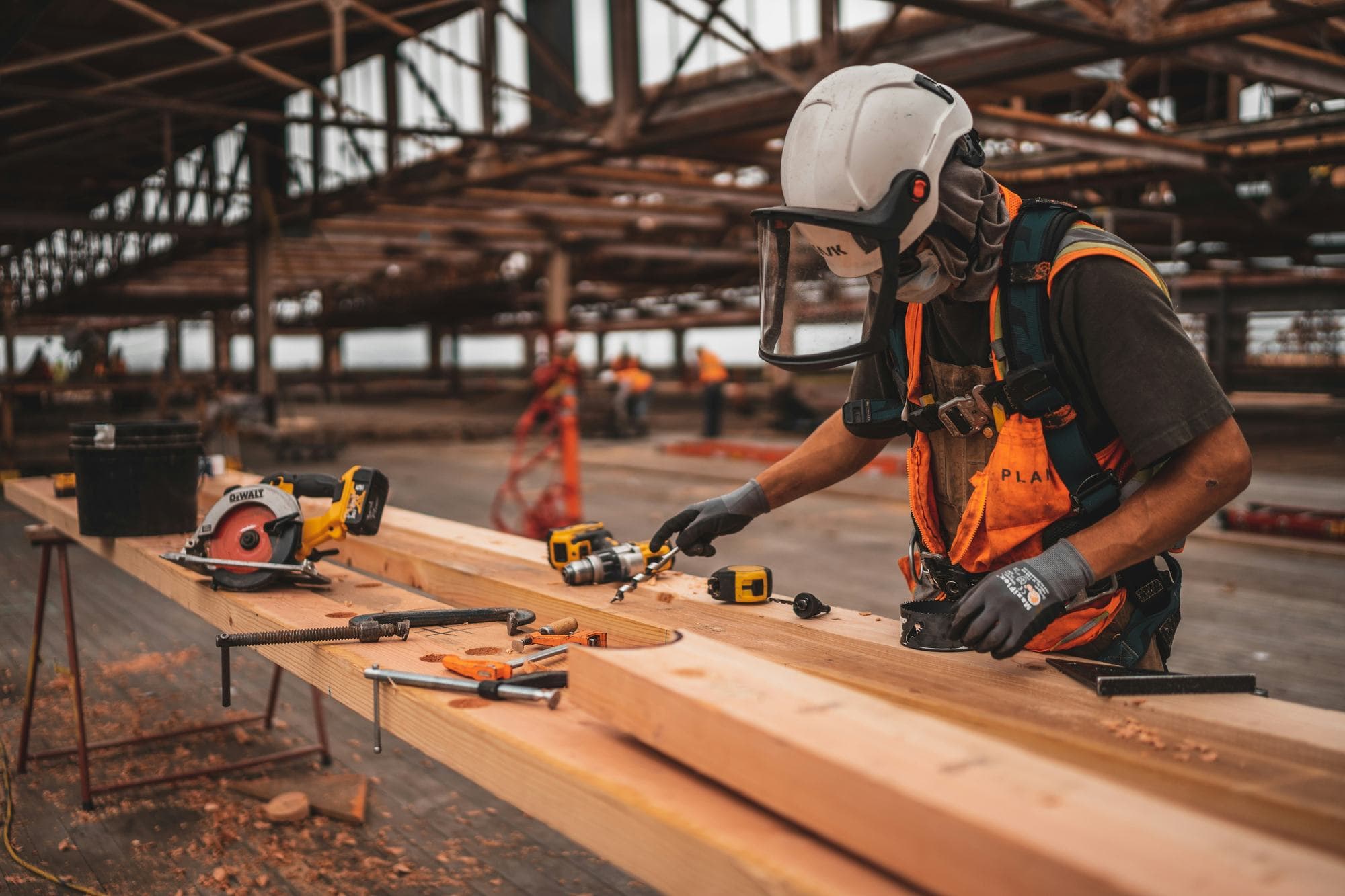 Builder in a hard hat and hi-vis measuring timber beams