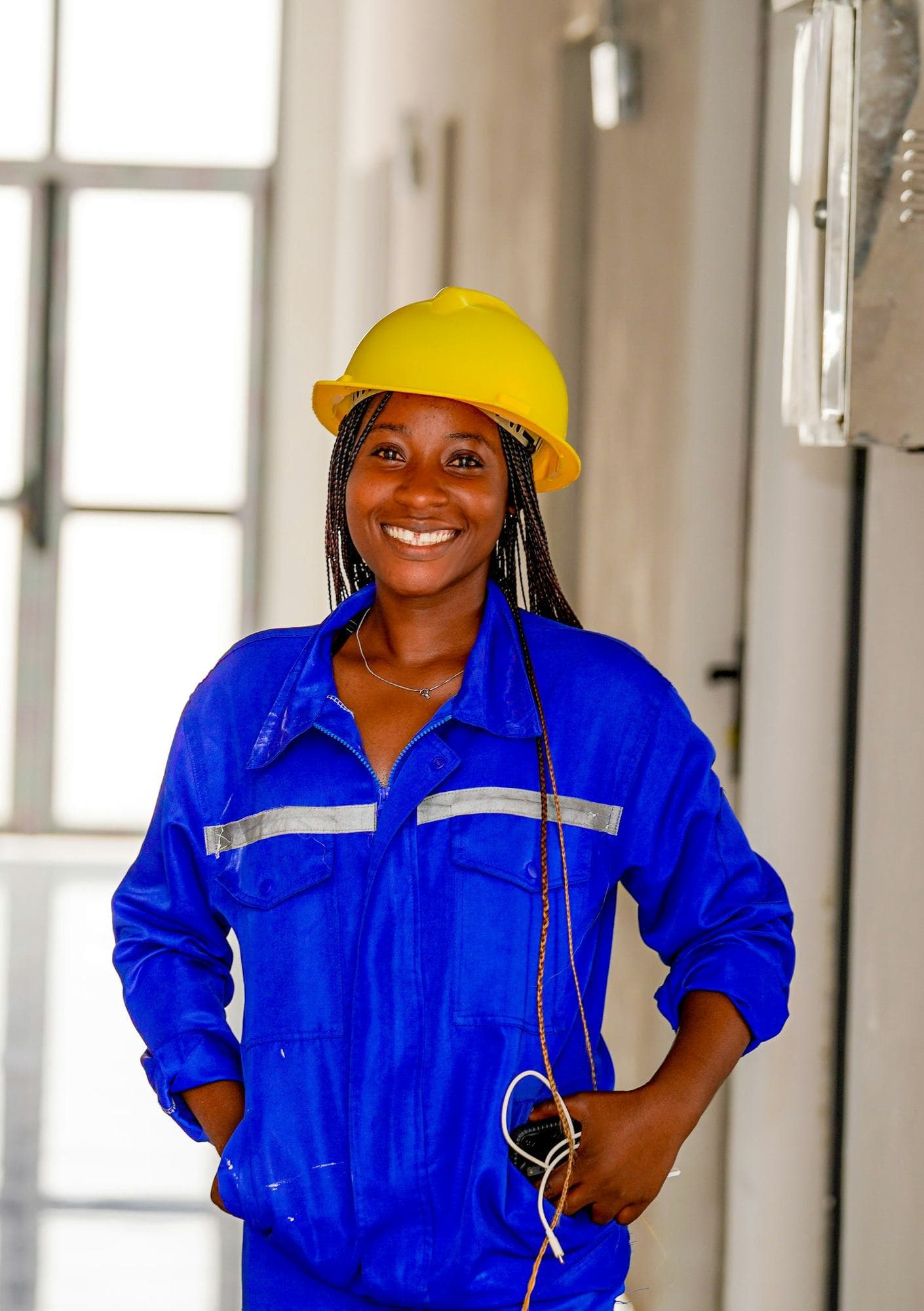 Smiling tradeswoman in blue overalls and a yellow hard hat